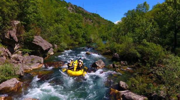 Eine Gruppe von Menschen raftet in einem gelben Schlauchboot auf einem Fluss mit Stromschnellen.