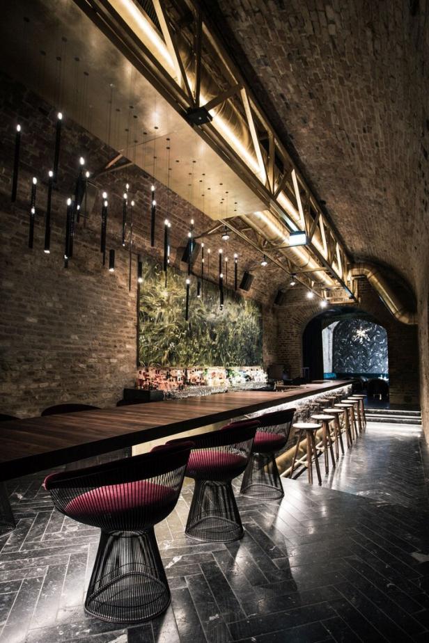 Eine Bar mit dunklen Holztischen und roten Stühlen in einem gewölbten Raum mit Ziegelwänden.