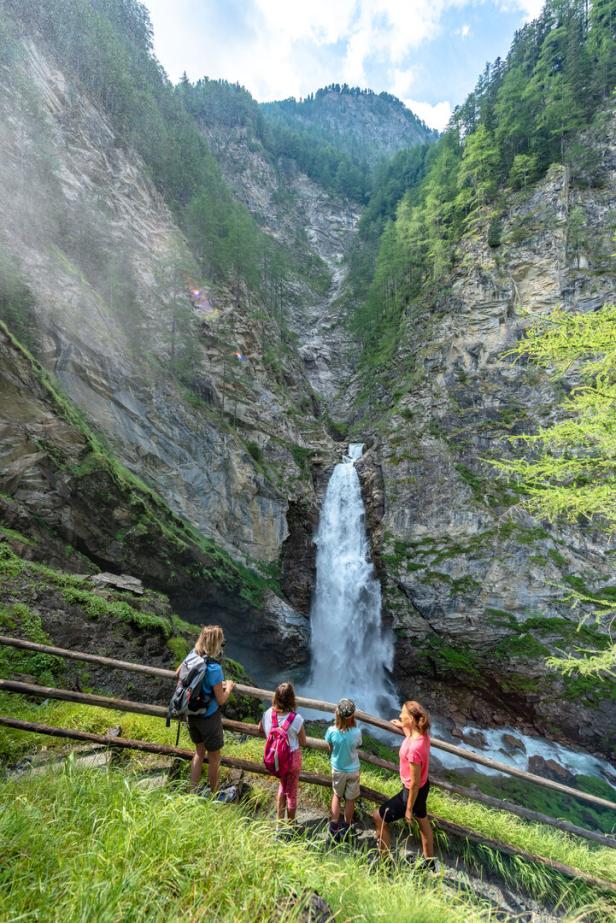Eine Familie genießt den Blick auf einen Wasserfall in einer felsigen Berglandschaft.