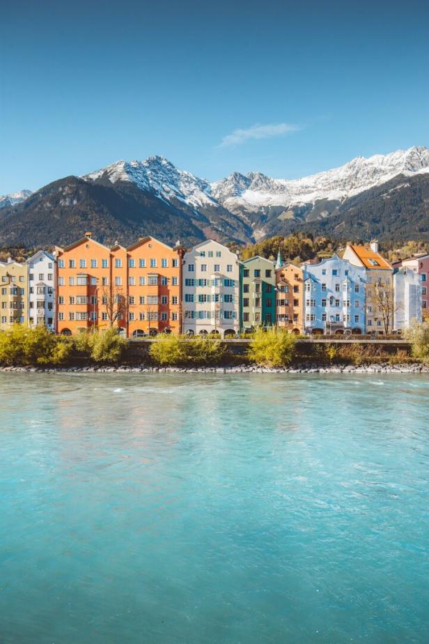 Bunte Häuserfassaden in Innsbruck vor einer Bergkulisse mit Schnee bedeckten Gipfeln.