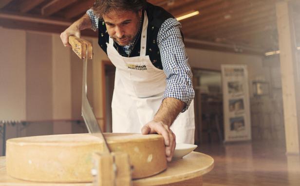 Ein Mann schneidet mit einem großen Messer ein Stück Käse an.