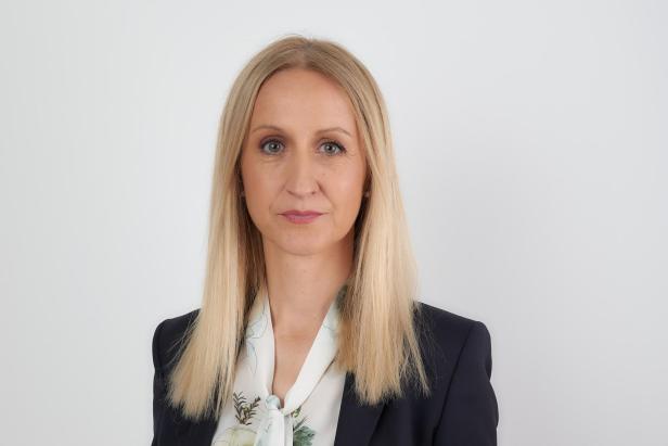 Porträt einer Frau mit blonden Haaren, die ein dunkles Jackett und eine helle Bluse trägt.