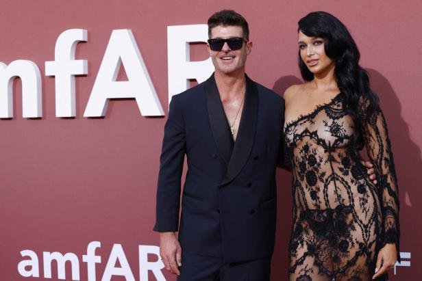 Robin Thicke und April Love Geary posieren auf einem roten Teppich vor dem amfAR-Logo.
