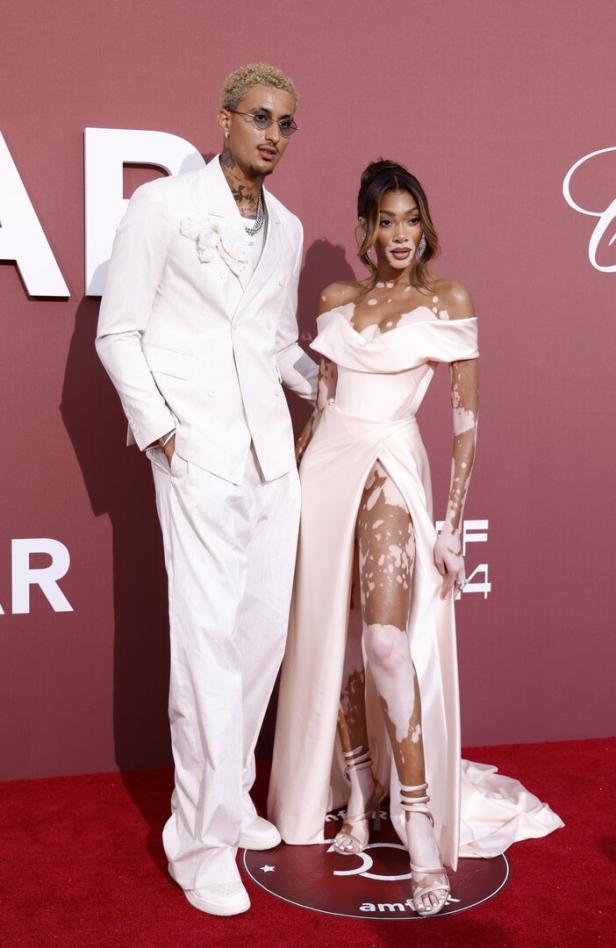 Model Winnie Harlow mit einem Mann in einem weißen Anzug auf einem roten Teppich.