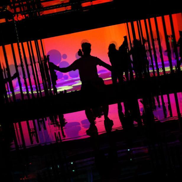 Silhouetten von Personen vor einer orangefarbenen und violetten Projektion.