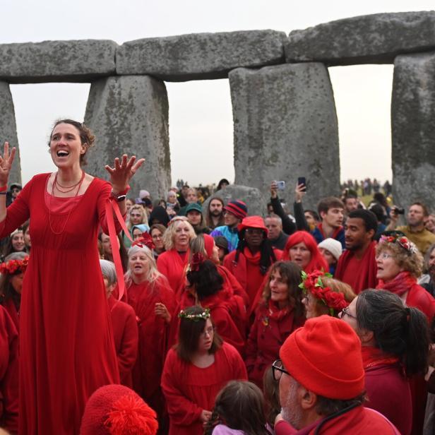 Eine Frau in Rot steht vor einer Menschenmenge in Stonehenge und gestikuliert.