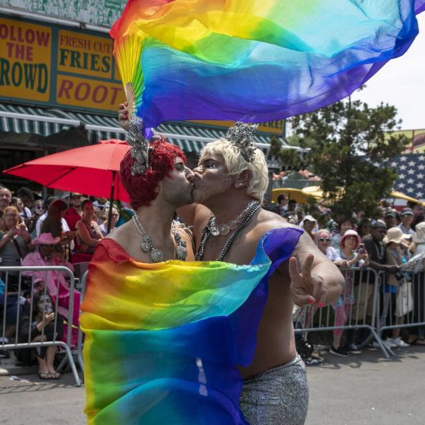 Zwei Männer, geschmückt mit Regenbogenfahnen und Kronen, küssen sich auf einer Pride-Veranstaltung.