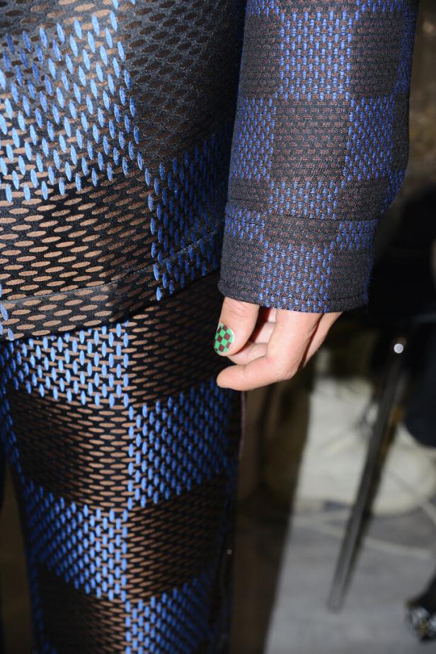 Detailaufnahme eines blau-schwarz gemusterten Kleidungsstücks mit einer Hand, deren Nagel grün-kariert lackiert ist.