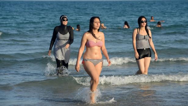 Drei Frauen unterschiedlichen Alters stehen im seichten Wasser eines Strandes.