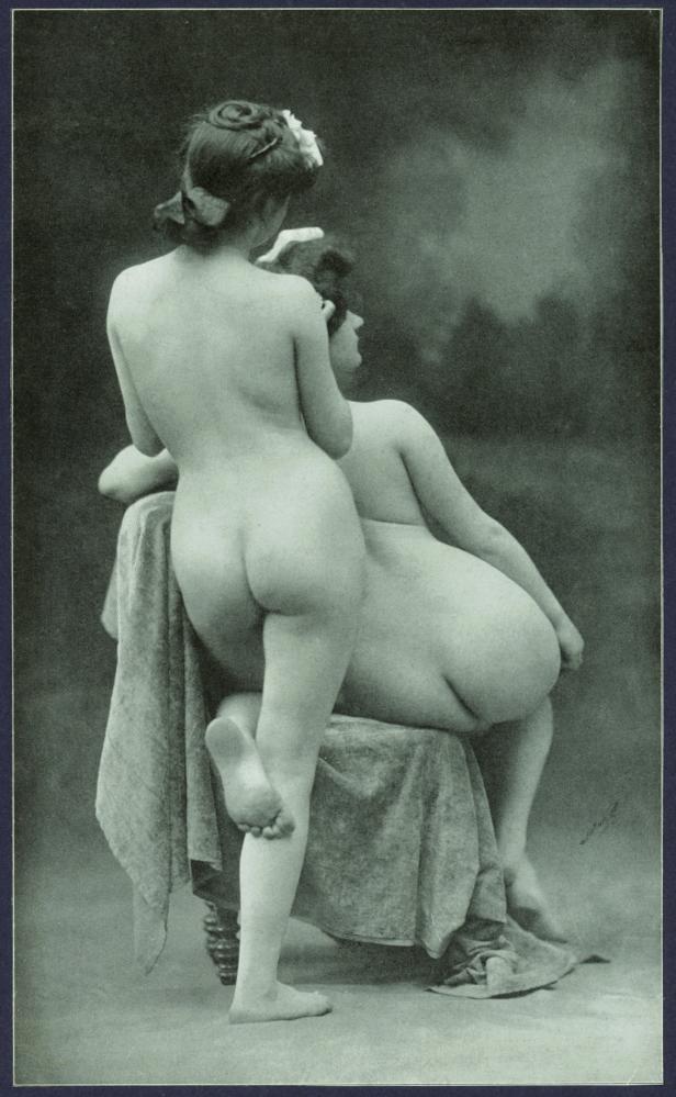 Zwei unbekleidete Frauen posieren auf einem Stuhl mit einem Tuch bedeckt.