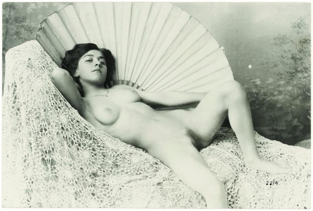 Eine junge Frau liegt nackt auf einer gehäkelten Decke, mit einem Fächer im Hintergrund.