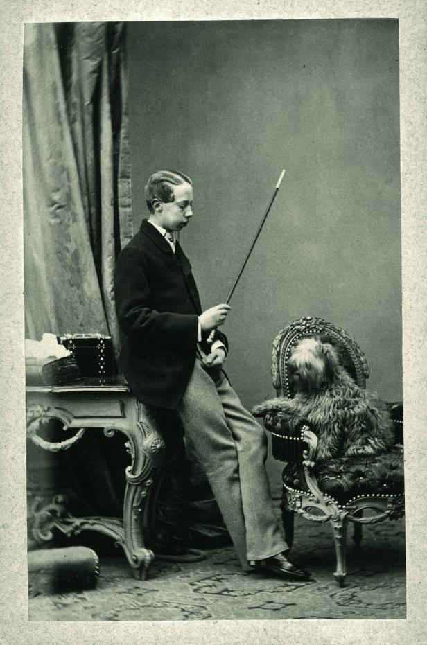 Ein junger Mann lehnt an einem Tisch, während ein Hund auf einem Stuhl sitzt.