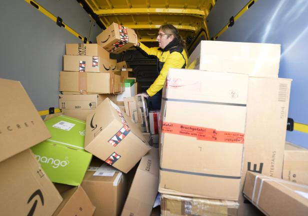 Eine Postzustellerin in gelber Jacke sortiert Pakete in einem Lieferwagen.