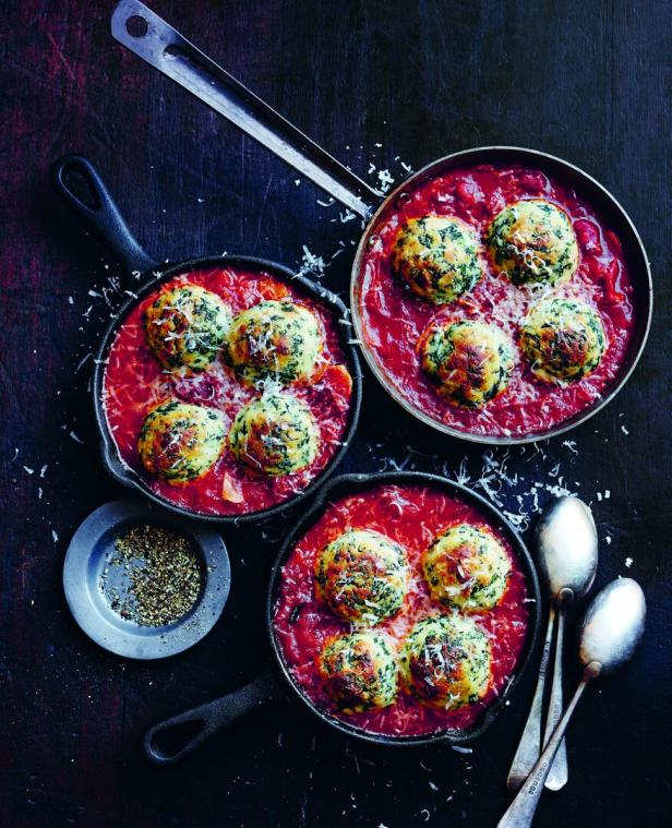 Drei Pfannen mit Spinatknödeln in Tomatensauce, bestreut mit Käse.