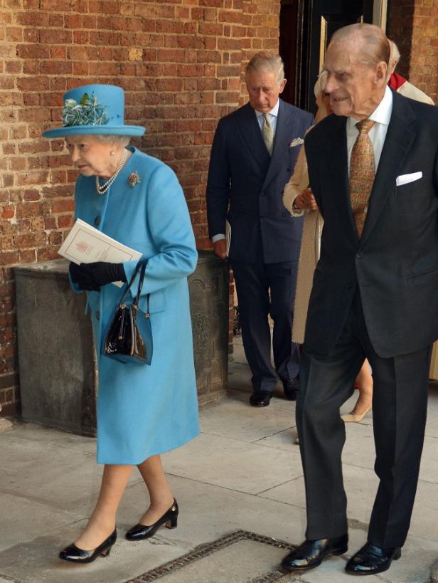 Königin Elisabeth II. in einem hellblauen Mantel mit Prinz Philip und Prinz Charles.