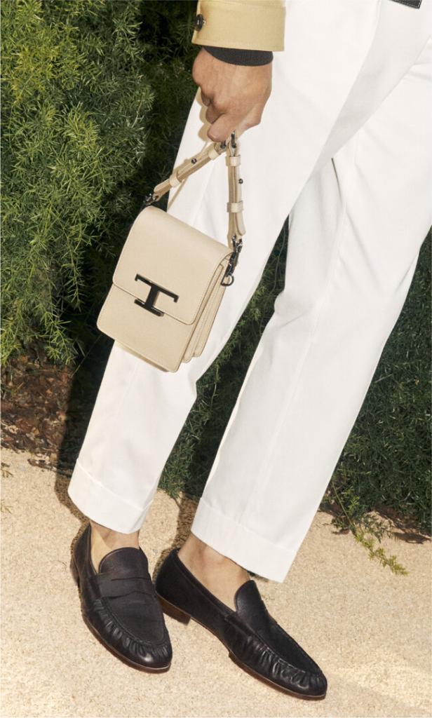 Eine Person in weißen Hosen und Lederschuhen hält eine Tod's Handtasche.