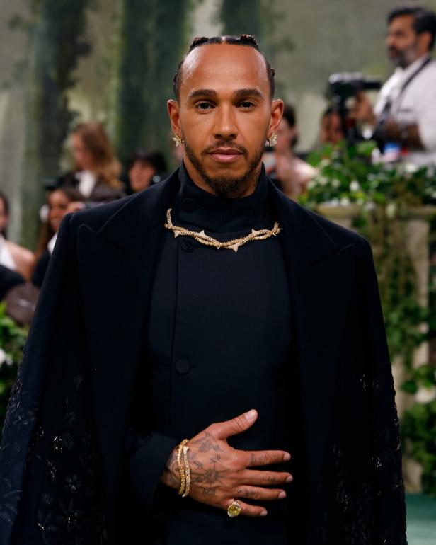 Lewis Hamilton trägt ein schwarzes Outfit mit goldenen Schmuckdetails.