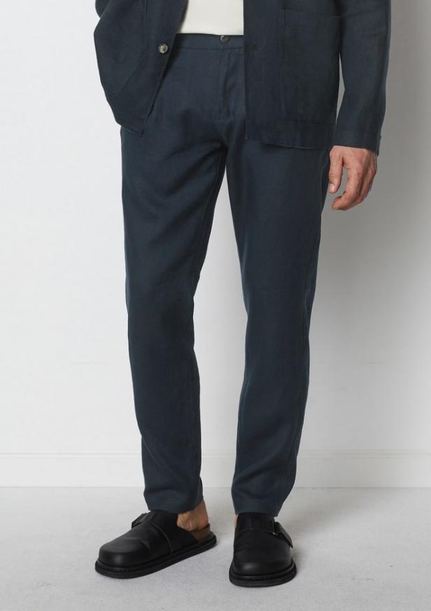 Eine Person trägt eine dunkelblaue Hose und schwarze Ledersandalen.