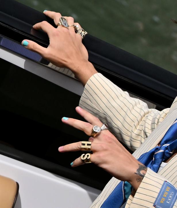 Die Hände einer Person mit mehreren Ringen und blau lackierten Fingernägeln.