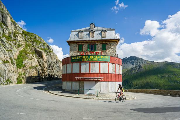 Gletscher Restaurant auf dem Furkapass in der Schweiz, Berglandschaft im Sommer, ein einzelner Fahrradfahrer auf der Straße