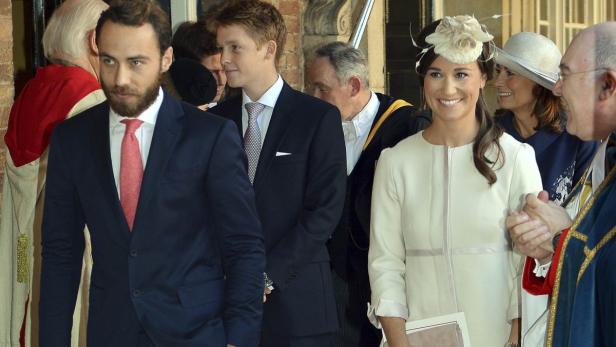 Pippa Middleton mit Hut und hellem Kleid bei einer Veranstaltung mit anderen Personen.