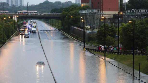 Eine überflutete Straße mit stehendem Wasser, in dem ein Auto fast vollständig versunken ist.