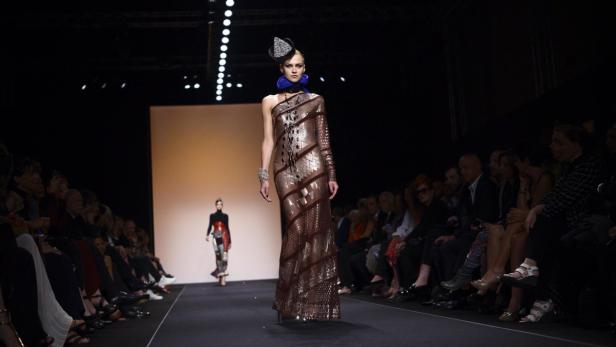 Eine Frau präsentiert ein langes, gemustertes Kleid auf dem Laufsteg einer Modenschau.