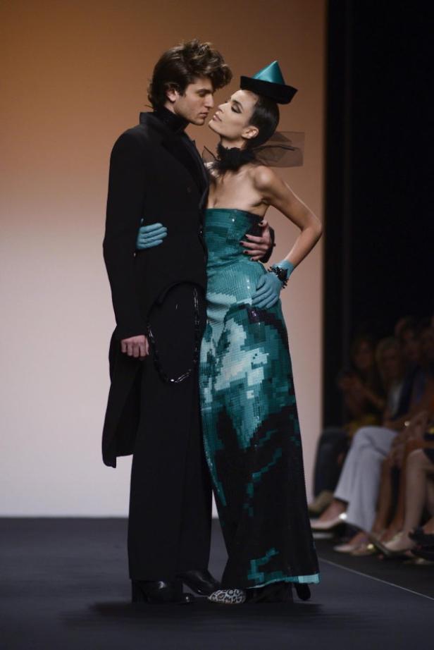 Ein Mann im Mantel umarmt ein Model in einem türkisfarbenen Kleid auf dem Laufsteg.