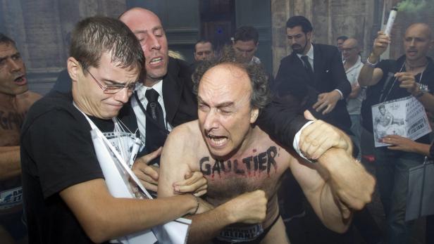 Ein Aktivist mit dem Wort „Gaultier“ auf der Brust wird von Sicherheitsleuten abgeführt.