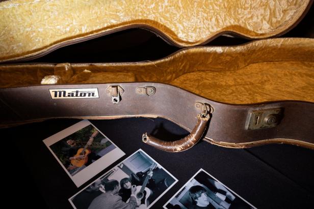 Ein geöffneter Gitarrenkoffer der Marke Maton mit alten Fotos davor.