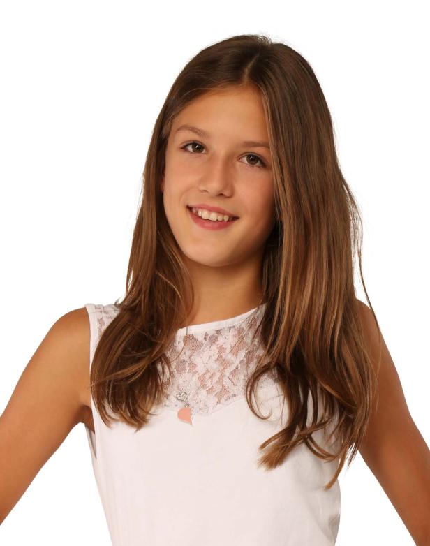 Ein junges Mädchen mit braunen Haaren und einem weißen Kleid lächelt.