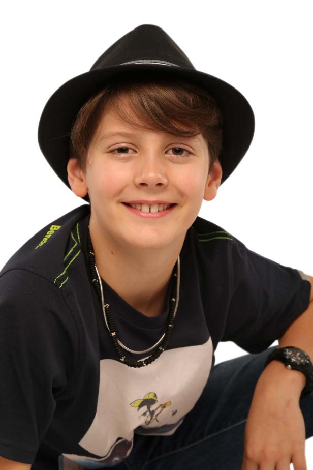 Ein lächelnder Junge mit Hut und Halskette vor einem weißen Hintergrund.