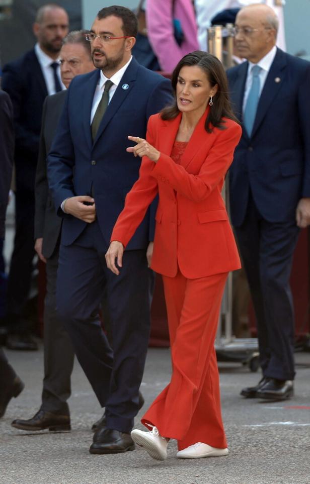 Königin Letizia in einem roten Hosenanzug und weißen Turnschuhen bei einem Auftritt.