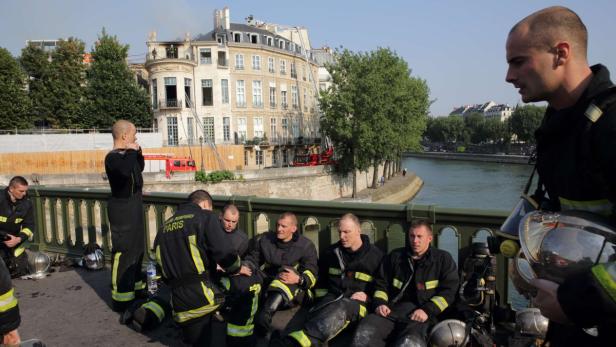 Eine Gruppe Pariser Feuerwehrleute ruht sich auf einer Brücke am Ufer der Seine aus.