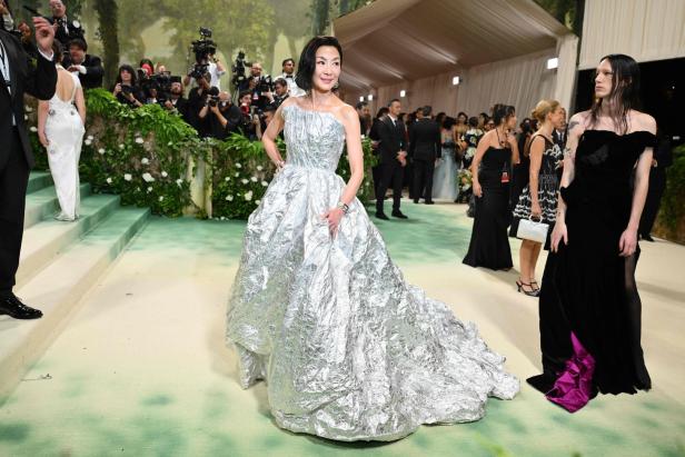 Michelle Yeoh in einer auffälligen silbernen Robe auf dem grünen Teppich.
