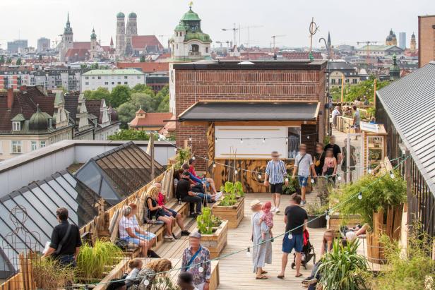 Menschen entspannen sich auf einer Dachterrasse mit Blick auf die Münchner Altstadt.