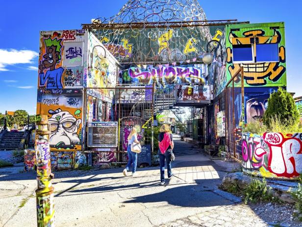 Zwei Frauen gehen durch eine Gasse, die mit Graffiti bemalten Containern gesäumt ist.