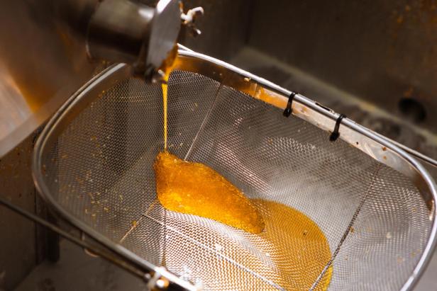 Eine goldene Flüssigkeit wird durch ein Metallsieb gegossen.