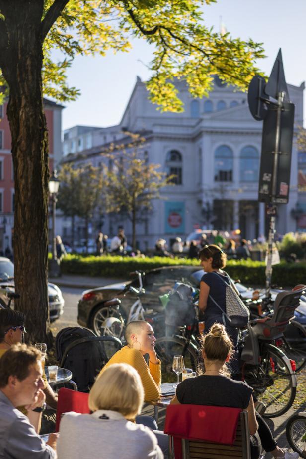 Menschen sitzen an Tischen vor einem Café in München.