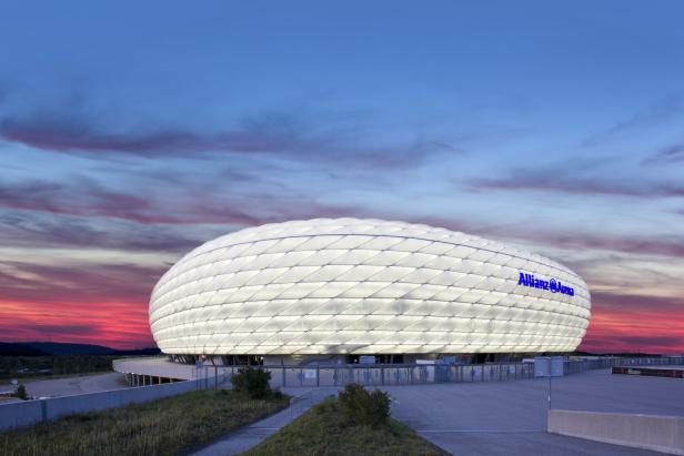 Die Allianz Arena in München leuchtet vor einem farbenprächtigen Abendhimmel.