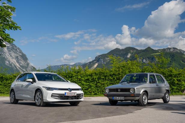 Ein neuer, weißer VW Golf steht neben einem älteren, silbernen VW Golf vor einer Bergkulisse.