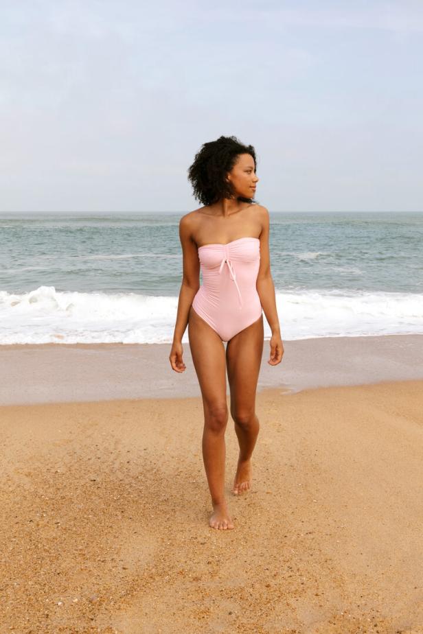 Eine Frau in einem rosa Badeanzug geht am Strand entlang.