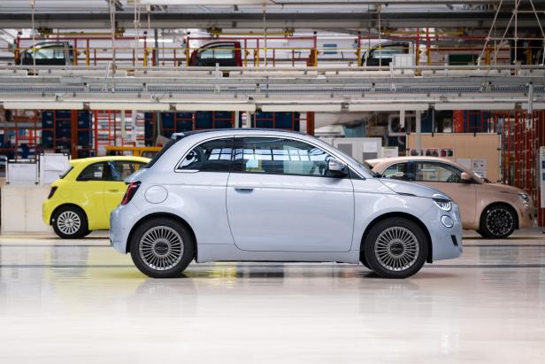 Ein hellblauer Fiat 500 steht in einer Fabrikhalle, im Hintergrund weitere Autos in Gelb und Rosa.