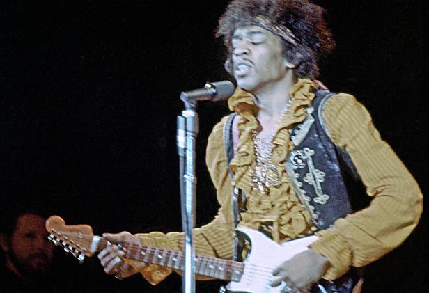 Jimi Hendrix spielt Gitarre und singt auf der Bühne.