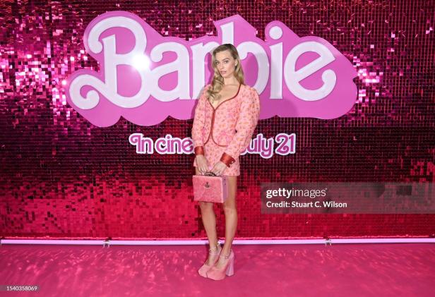 Margot Robbie posiert vor einem „Barbie“-Filmposter.