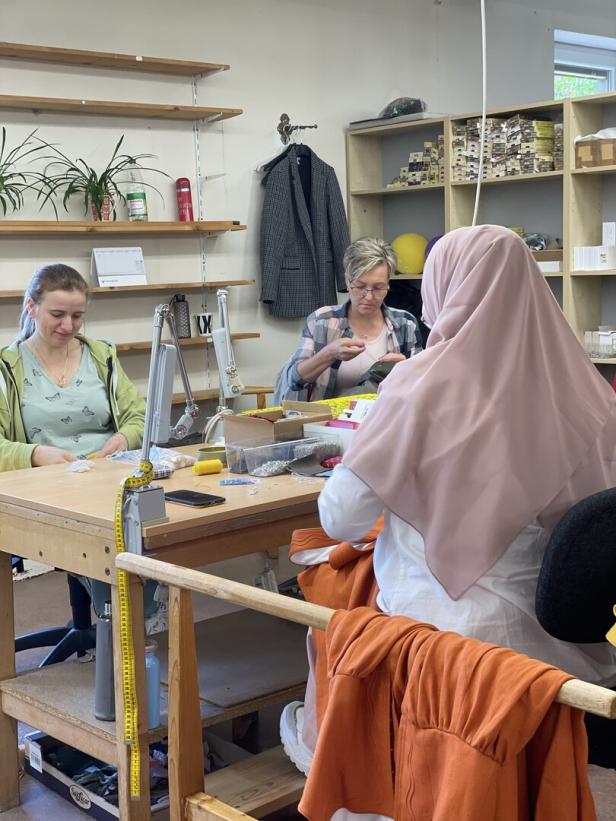 Drei Frauen sitzen an einem Tisch und arbeiten an Textilien.