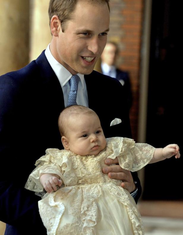 Prinz William hält ein Baby in einem verzierten Taufkleid.