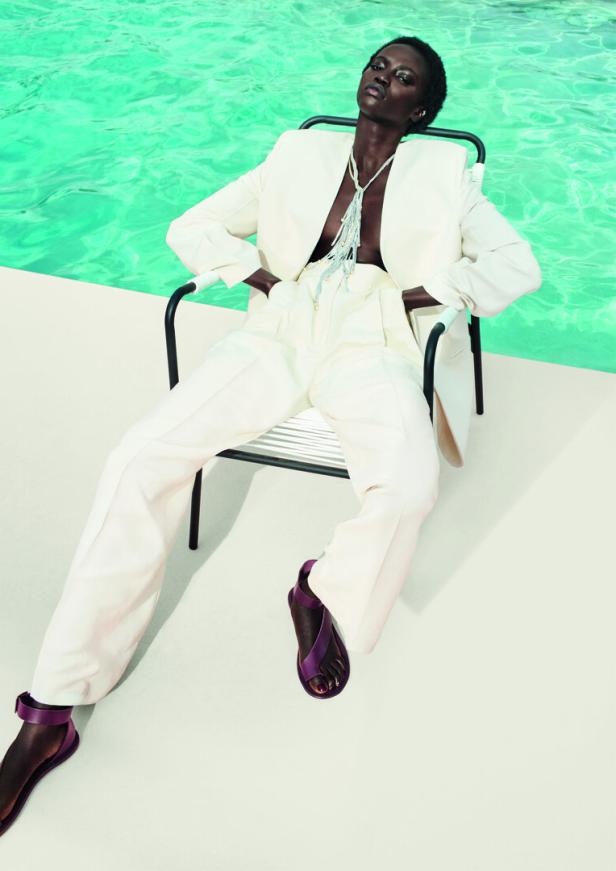 Eine Frau in einem weißen Hosenanzug sitzt an einem Pool.