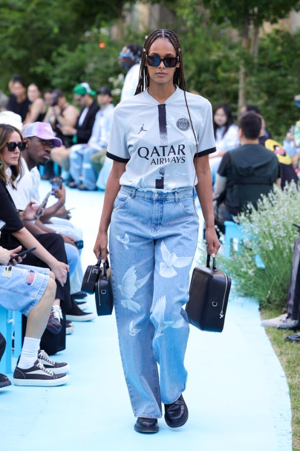 Eine Frau in Jeans mit Taubenmuster und einem Paris Saint-Germain Trikot auf einem Laufsteg.