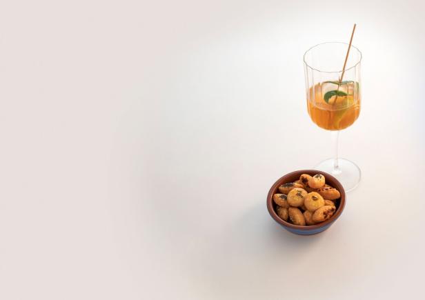 Ein Aperol-Spritz in einem Glas mit einer Schale salzigem Gebäck auf einem Tisch.